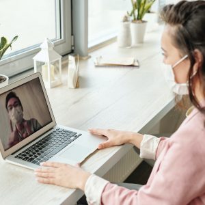 a woman wearing mask video calling with colleague on laptop