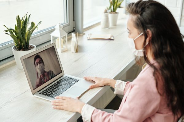 a woman wearing mask video calling with colleague on laptop